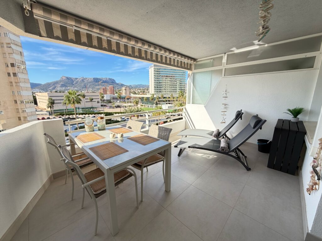 Overdekt balkon met eettafel en ligstoelen, met uitzicht over Calpe en de bergen